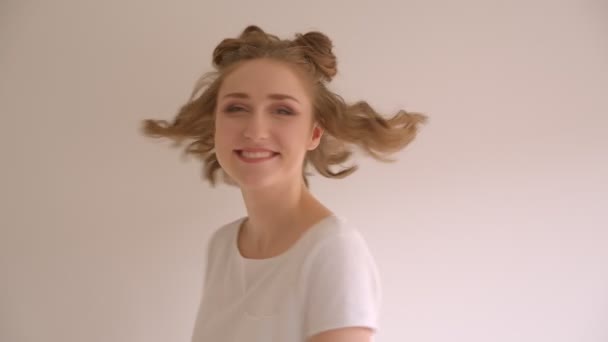 Closeup shoot of young cute caucasian female with hair buns smiling and laughing happily turning to camera in the white room indoors - Footage, Video