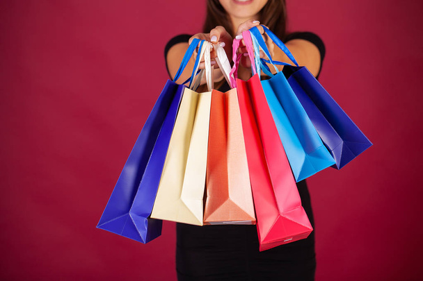 Zakupy. Kobieta trzyma kolorowe torby na czerwonym tle w czarnym piątek wakacje - Zdjęcie, obraz