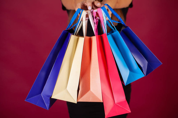 Shopping. Woman holding colored bags on red background in black friday holiday - Foto, Imagen