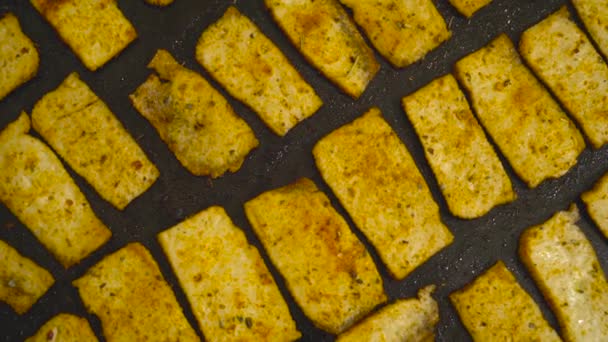 Close-up van gebakken tofu met specerijen op een bakplaat. Gezond dieet vegetarisch en veganistisch eten. Gebakken tofu op een zwarte achtergrond. - Video