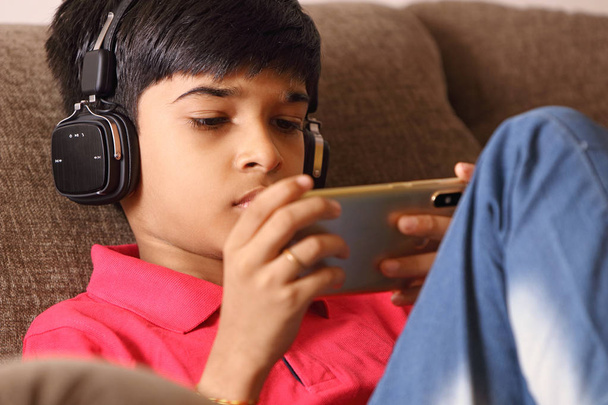 インドの若いです男の子リッスン音楽とともにヘッドフォンと保持携帯電話 - 写真・画像