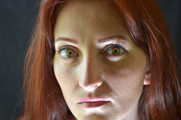 Menina branca com cabelos vermelhos e olhos verdes com extensões de pestanas em um fundo escuro parece emocionalmente assustador
 - Foto, Imagem