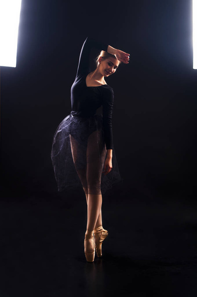 Charming girl ballerina in a black suit, is dancing a ballet in the light of the contour . - Fotografie, Obrázek