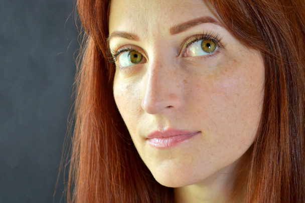 Fehér lány vörös hajjal és zöld szemekkel, szempilla hosszabbítókkal sötét háttérrel, felnéz balra. - Fotó, kép