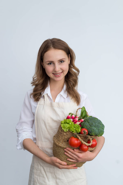 A woman holds different vegetables in a basket on a light background. The concept of vegetarian food. - Foto, Imagen
