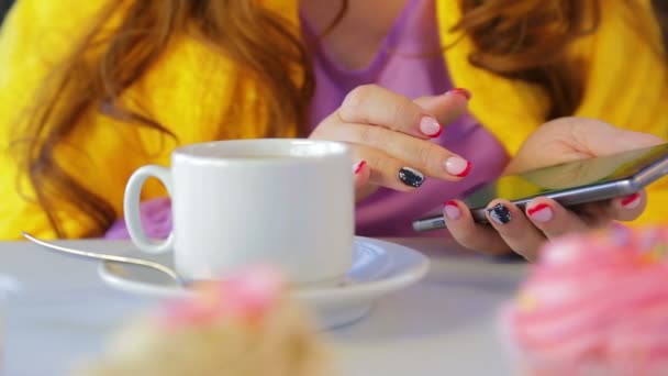 The girl in a cafe at the table with cakes leafing through the news in the smartphone - Кадри, відео