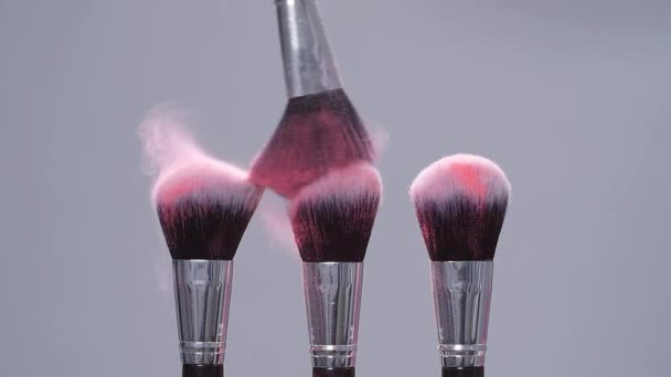 Cepillo de maquillaje con salpicaduras de polvo rosa explosión sobre fondo gris en cámara lenta
 - Metraje, vídeo