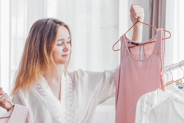 Woman can not choose which clothes pack for travel. Clothing, fashion, style and people concept - woman choosing clothes at home wardrobe.  - 写真・画像