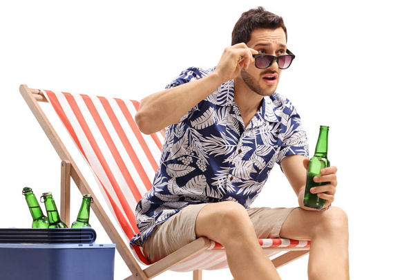 Young guy with a beer bottle sitting in a deck chair and staring - Foto, immagini