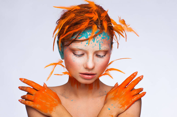 Portrait of a beautiful model with creative make-up and hairstyle using orange feathers - 写真・画像