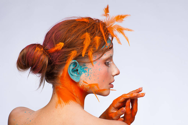 Portrait of a beautiful model with creative make-up and hairstyle using orange feathers - Fotografie, Obrázek