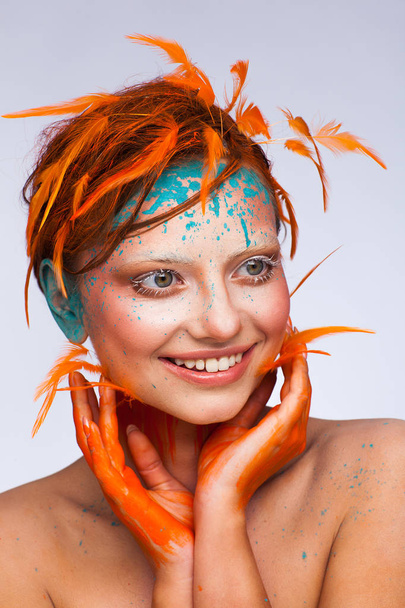 Portrait of a beautiful model with creative make-up and hairstyle using orange feathers - Foto, Bild