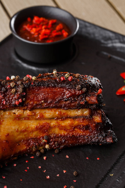 Grilled and barbecue hot pork ribs with hot chilli pepper and hot sauce on black stone background. Isolated. Dish for men. Spicy - Foto, Imagem