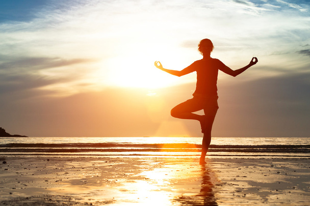 Sylwetka kobieta ćwiczy jogę na plaży o zachodzie słońca. - Zdjęcie, obraz