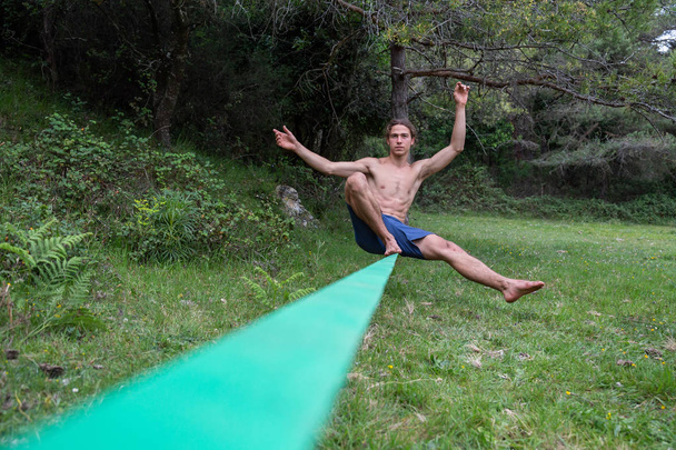 Jovem ativo com tronco nu equilibrando no slackline no campo verde no verão
 - Foto, Imagem