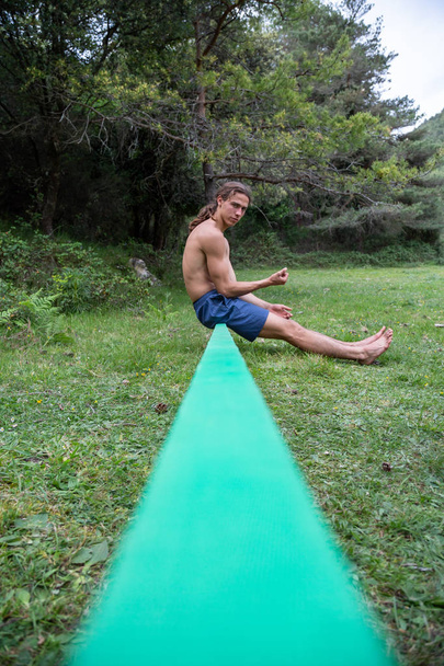 Jovem ativo com tronco nu equilibrando no slackline no campo verde no verão
 - Foto, Imagem