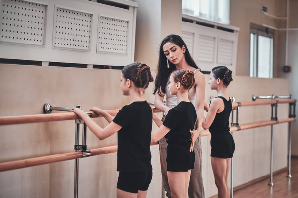 Талантливый тренер показывает молодым девушкам, как делать балетные упражнения
 - Фото, изображение
