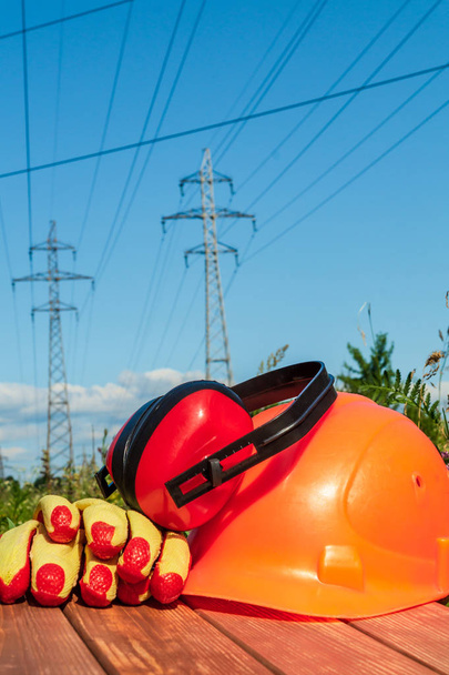 Protective helmet, headphones, gloves on a wooden table, against the background of nature and high voltage posts.. - Photo, Image