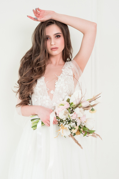 Portrait of a beautiful bride with a wedding bouquet. Brunette girl with curly hair and fashion makeup. - Foto, afbeelding