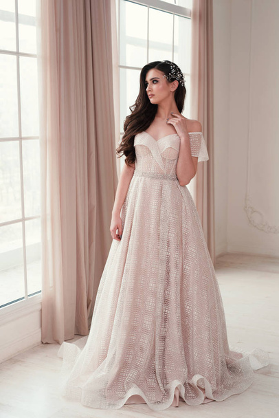 パノラマの窓の近くに豪華なウェディングドレスを身に着けているスリム美しい女性。花を持つ豪華な花嫁. - 写真・画像