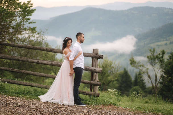 Sevimli gelin dağlarda onu yakışıklı damat sarılmak. Güzel düğün çift yürüyüş. Yeşil gackground - Fotoğraf, Görsel
