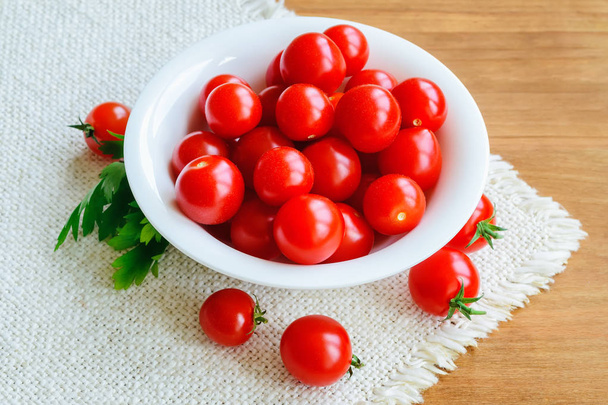 Red ripe cherry tomatoes in white bowl and parsley on fringed table napkin - Zdjęcie, obraz