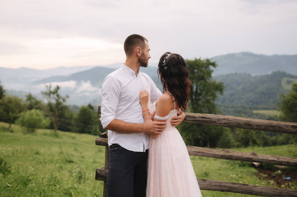 Encantadora novia abrazar a su novio guapo en las montañas. Hermosa pareja de boda a pie. Terreno de juego verde
 - Foto, imagen