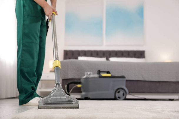 Professional janitor removing dirt from carpet with vacuum cleaner in bedroom, closeup. Space for text - Фото, зображення