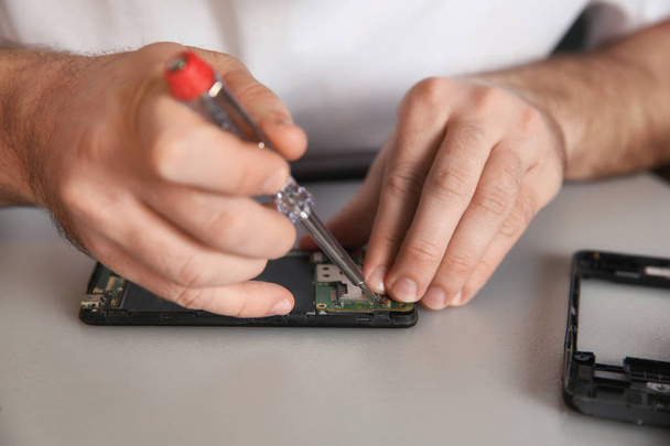 Technician repairing mobile phone at table, closeup - Фото, изображение