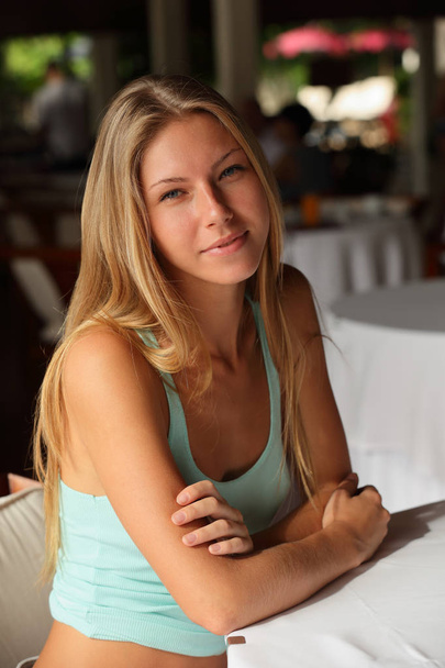 Portrait of a happy and smiling attractive young adult blonde woman with beautiful bare hands sitting at a table with a white tablecloth - Fotó, kép
