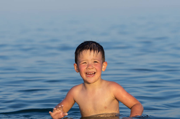 3歳の男の子が弟と一緒に日没時に海で泳いでいます. - 写真・画像