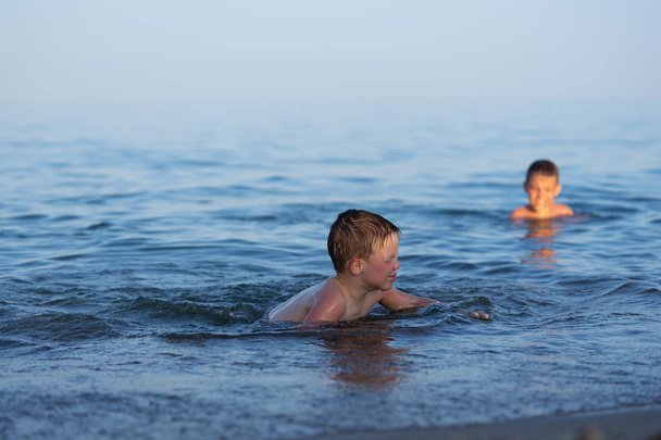 Un niño de tres años está nadando en el mar al atardecer con su hermano
. - Foto, imagen