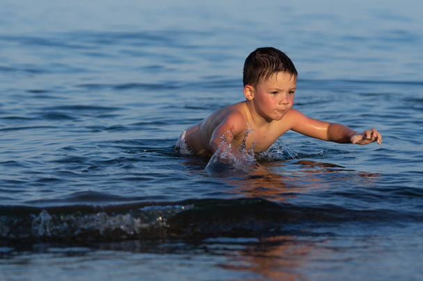 A boy of three years is swimming in the sea at sunset with his brother. - Photo, Image