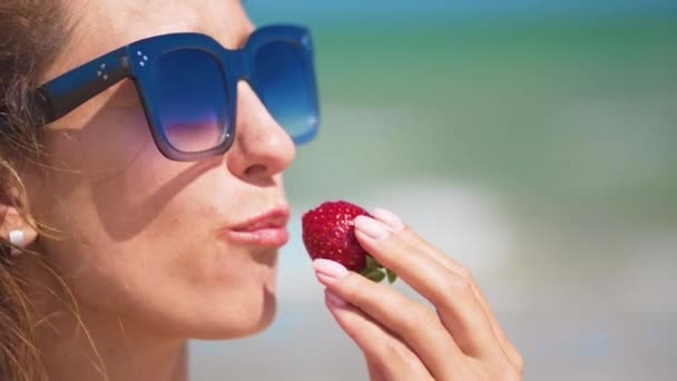 Donna che mangia fragole vicino al mare nella soleggiata giornata estiva. Primo piano
. - Filmati, video