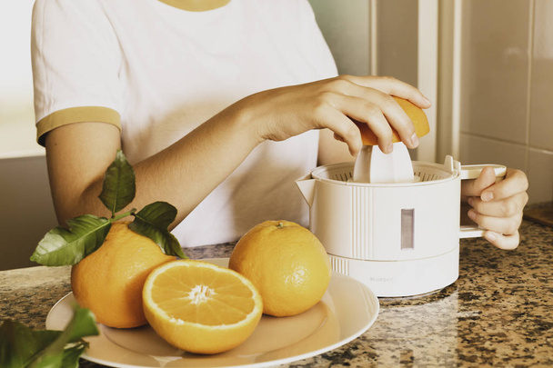 Деталь рук подростка, держащего цитрусовую соковыжималку с апельсиновой половинкой и свежевыжатыми цитрусовыми
 - Фото, изображение