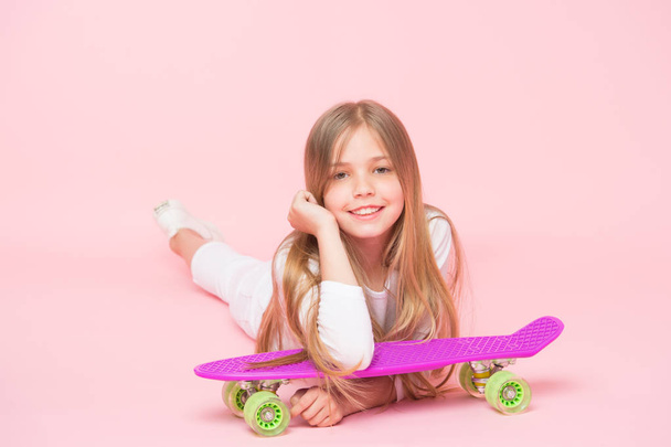 An extreme child. Small child relaxing at skateboard on pink background. Cute little child with violet penny board. Adorable girl child with skater style and look - Foto, imagen