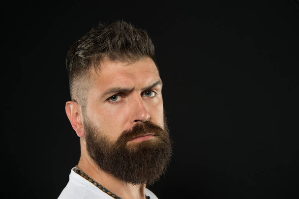 Bring more style to bearded face. Bearded man on black background. Serious bearded hipster with stylish haircut. Brutal caucasian guy wearing mustache and beard on bearded face, copy space - Photo, image