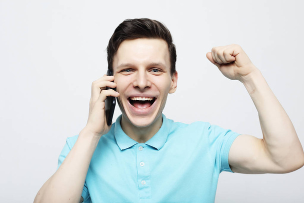 Happy young man in shirt gesturing and smiling while talking on the mobile phone - Foto, imagen