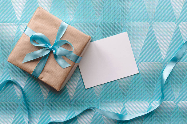 Geschenkverpackung in braunem Papier mit Schleife auf blauem Hintergrund mit Grußkarte. Attrappe - Foto, Bild