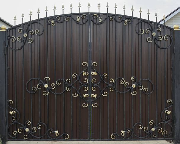 Ozdobny i piękny drzwi ogrodzenia z kutego żelaza malowane szkarłatny brązowy i złoto. Zdjęcie naturalnej starej bramy do wykorzystania jako tekstura - Zdjęcie, obraz