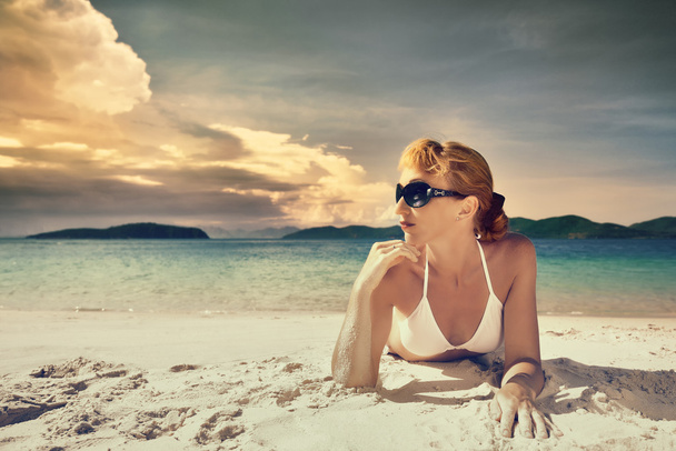 Uma mulher bonita de biquíni tomando banho de sol na praia em um fundo
 - Foto, Imagem