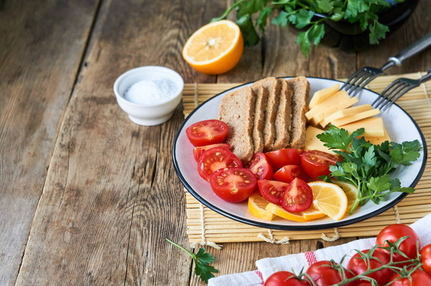 Plate of cherry tomatoes, cheese and rye bread on a wooden background                                - Foto, immagini