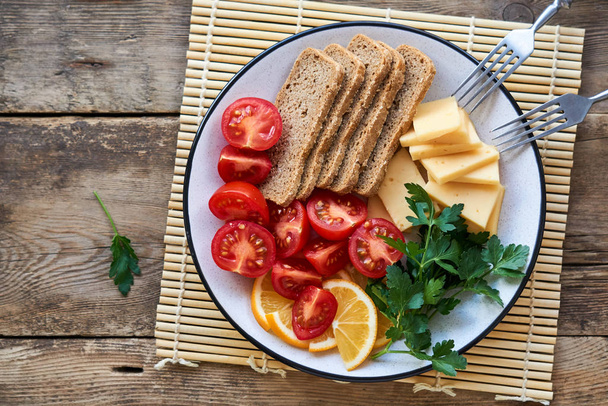 Plate of cherry tomatoes, cheese and rye bread on a wooden background                                - Foto, immagini