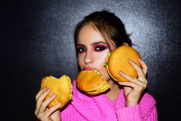 Fashion, beauty.Sexy woman with perfect makeup eating hamburgers. Female beauty visage concept. - Фото, зображення