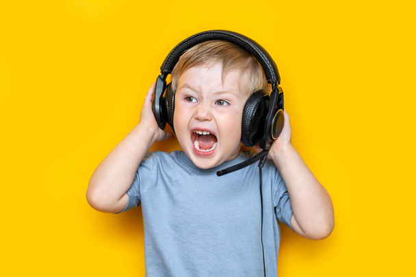 handsome little boy in modern headphones and shouting while standing on yellow background - Photo, Image