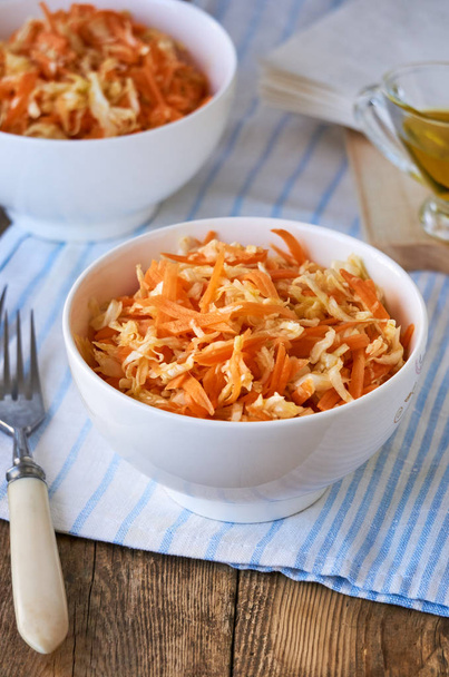 Salad with fresh cabbage, carrots and olive oil in a white bowl on a wooden background                                - Foto, imagen