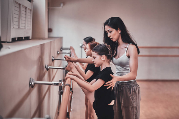 Erfahrene Ballettlehrerin zeigt jungen Mädchen, wie man wichtige Übungen macht - Foto, Bild