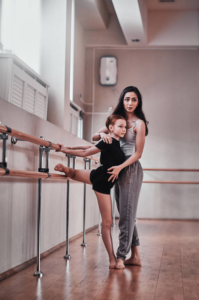 Молодая задумчивая девушка проходит специальную балетную подготовку у прилежного тренера
 - Фото, изображение