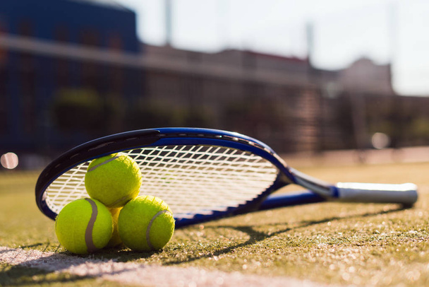 drei Tennisbälle und Schläger auf Hartplatz im Sonnenlicht - Foto, Bild