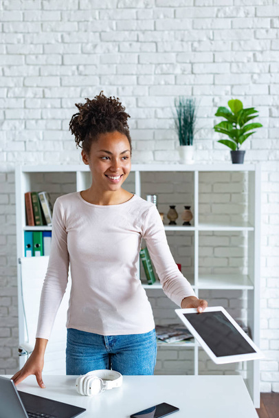 Cheerful mulatto woman takes the tablet in office looking straight.- Image - Φωτογραφία, εικόνα